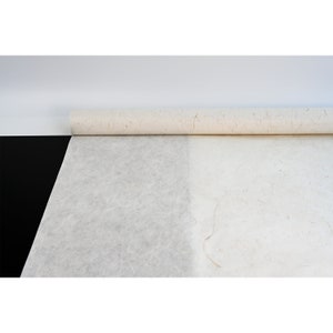 Pu&ograve; includere: Un rotolo di carta bianca testurizzata con un aspetto di fibra naturale. La carta &egrave; arrotolata e parzialmente srotolata, rivelando la texture della carta.