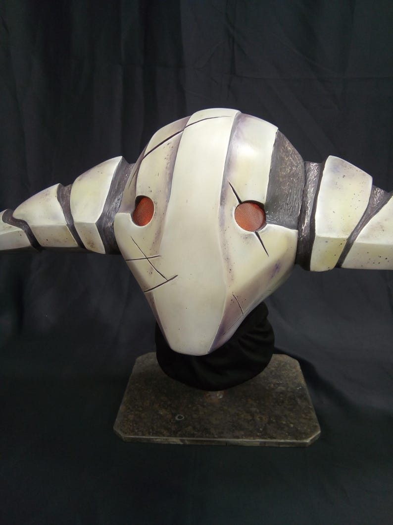 May include: A white and gray mask with red eyes and a striped design. The mask is on a black stand.