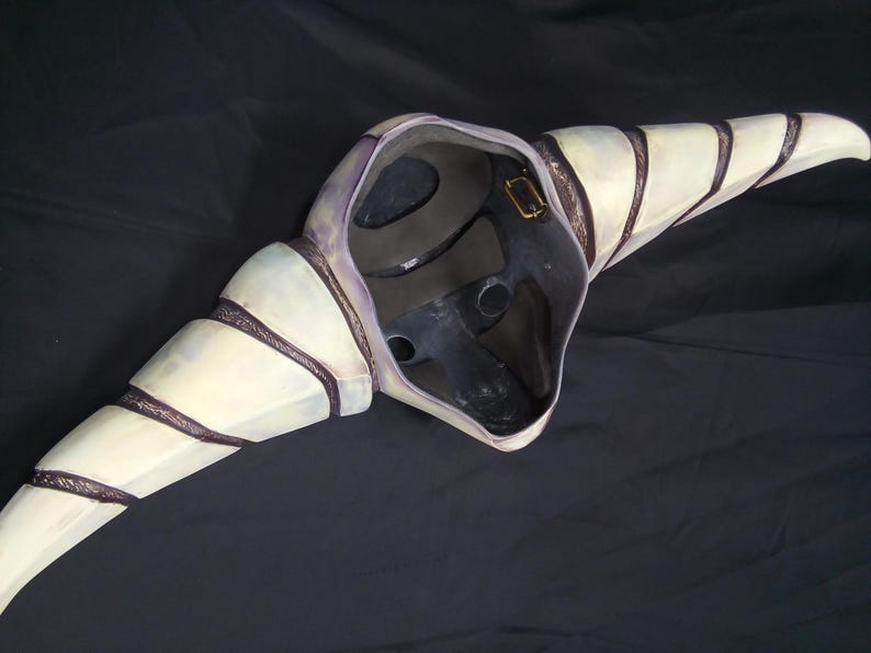 May include: A white and purple mask with black stripes and a textured surface. The mask has a large beak and a hole for the eyes.
