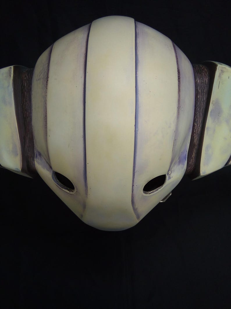May include: A white helmet with purple stripes and two eye holes. The helmet is made of a hard material and has a smooth surface.