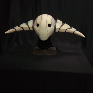 May include: A white and black mask with horns, resembling a creature from a fantasy world. The mask has a textured surface and two eye holes.