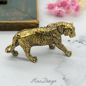 May include: A gold-colored metal figurine of a tiger walking. The tiger has detailed fur and a curled tail.