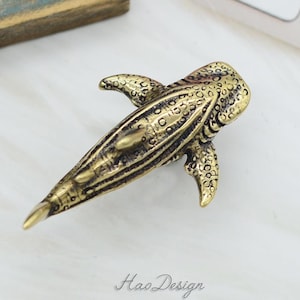 May include: A gold-colored metal figurine of a whale shark. The figurine is detailed with textured scales and fins.