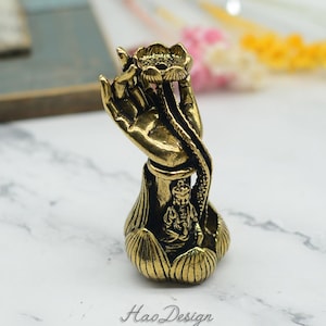 Peut inclure: Un brûle-encens en métal doré en forme de main tenant une fleur de lotus. Une petite figurine est assise à l'intérieur du lotus.