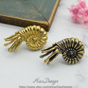 May include: A pair of gold-toned ammonite earrings with a detailed, textured design. The earrings are a unique and stylish accessory for any occasion.