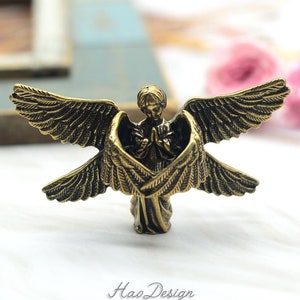 May include: A small golden angel figurine with outstretched wings, praying with hands clasped together. The angel is standing on a white surface.