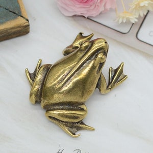 May include: A small, gold-colored brass frog figurine. The frog is sitting with its mouth open and its eyes closed. The figurine is detailed and realistic.