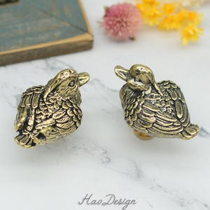 Peut inclure: Deux tirettes de tiroir en forme de canard dorées. Les canards sont tournés dans des directions opposées et présentent des motifs de plumes détaillés.