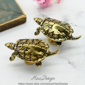 Op de afbeelding: Twee gouden schildpadvormige ladegrepen. De schildpadden zijn gedetailleerd met getextureerde schalen en hebben een realistisch uiterlijk.