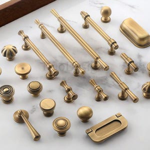 May include: A collection of antique brass cabinet hardware, including knobs, pulls, and a recessed handle. The hardware features various designs, from simple round knobs to ornate pulls, all in a warm, aged brass finish.