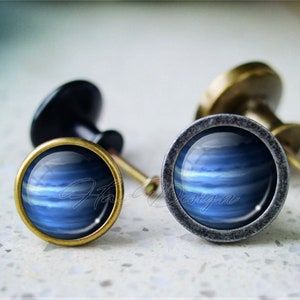 May include: Two cabinet knobs with a blue and white abstract design. The knobs are made of metal and have a brass finish.