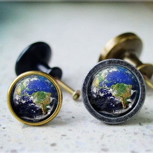 Puede incluir: Dos pomos de armario con un diseño redondo de globo azul y verde. Los pomos son de metal y tienen un aspecto vintage.