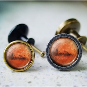 Puede incluir: Dos pomos de armario con acabado en bronce. Los pomos tienen un inserto redondo de vidrio con una imagen de Marte.