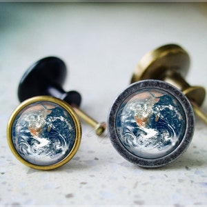 May include: Two cabinet knobs with a blue and brown globe image on the front. The knobs are made of metal and have a vintage look.