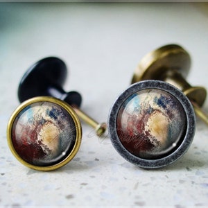 May include: Two decorative cabinet knobs with a round, brass base and a gray metal ring. The knobs feature a colorful, abstract design with shades of red, blue, and yellow.