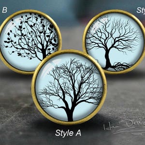 Op de afbeelding: Drie ronde, goudkleurige, decoratieve ornamenten met een blauwe achtergrond en een zwart silhouet van een boom. De bomen hebben verschillende stijlen van takken en bladeren. De ornamenten zijn gelabeld met "Style A", "Style B" en "Style C".