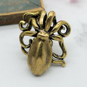 Może przedstawiać: Szczegółowy pierścionek w kształcie ośmiornicy w stylu antycznym, w brązowym wykończeniu. Pierścionek posiada teksturowany korpus i kręcone macki, tworząc unikalny i przyciągający wzrok design. Pierścionek jest umieszczony na białym tle z tekstem "Hao Design" i adresem strony internetowej.