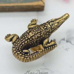May include: A gold-toned alligator-shaped cabinet knob or drawer pull. The alligator is detailed with textured scales and has a raised tail.