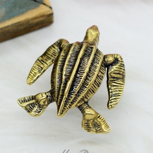 Op de afbeelding: Een gouden metalen schildpadfiguur met een gedetailleerde, getextureerde schil. De schildpad bevindt zich in een looppositie met zijn kop en poten uitgestoken.