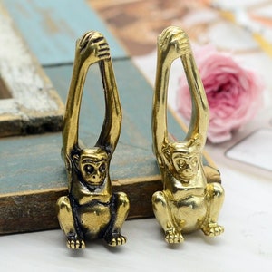 Könnte beinhalten: Zwei goldene Affenfiguren mit erhobenen Armen. Die Affen sitzen auf einer Holzoberfläche.