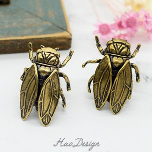 Könnte beinhalten: Ein Paar goldfarbene Zikaden-Ohrringe. Die Ohrringe sind detailliert und realistisch, mit filigranen Flügelmustern.