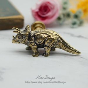 Peut inclure: Une poignée de porte en laiton doré en forme de Tricératops. Le dinosaure a une surface texturée et une longue queue.