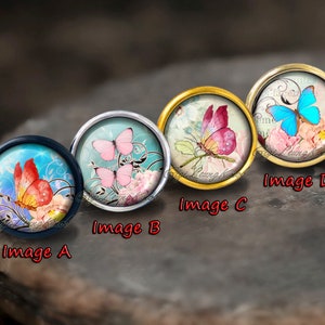 Puede incluir: Cuatro cabujones redondos de vidrio con diferentes dise&ntilde;os de mariposas. Los cabujones est&aacute;n engastados en monturas met&aacute;licas. Las mariposas est&aacute;n pintadas en tonos de rosa, azul y naranja. Los cabujones est&aacute;n rodeados de un dise&ntilde;o floral.