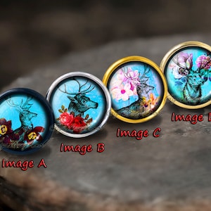Puede incluir: Cuatro cabujones redondos de vidrio con diferentes imágenes de un ciervo con cuernos y flores sobre un fondo azul. Los cabujones están engastados en engastes de plata, oro y negro.