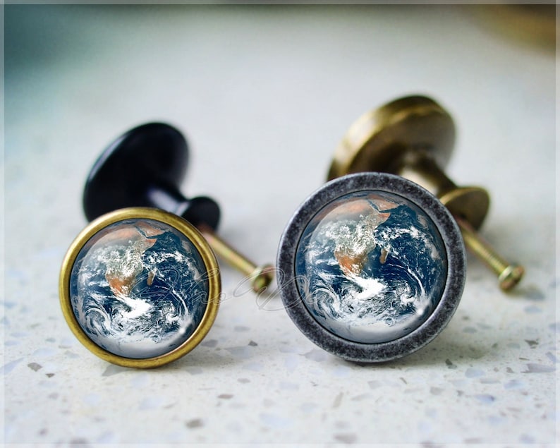 以下が含まれることがあります： 前面に青と茶色の地球儀の画像が描かれたキャビネットノブが2つ。ノブは金属製で、ビンテージな外観です。