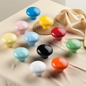 Op de afbeelding: Een verzameling kleurrijke keramische kastknoppen in diverse tinten, waaronder blauw, geel, roze, rood, groen, zwart, wit en oranje. De knoppen hebben een glanzende afwerking en een afgeronde vorm, perfect voor het opfleuren van meubels.