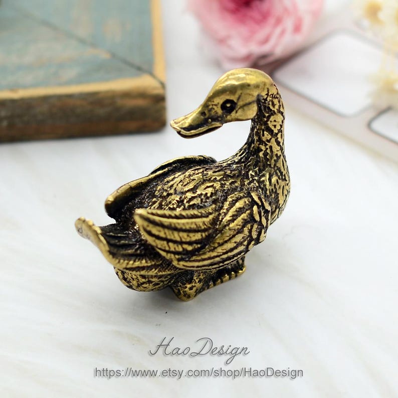 May include: A small, gold-coloured brass duck figurine with detailed wings and a textured surface.