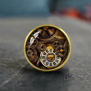 May include: A round, brass-colored pendant with a glass dome featuring a steampunk-inspired design of gears and a clock face with Roman numerals.