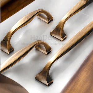 May include: Close-up of four antique bronze cabinet pulls. The pulls have a curved handle design with a rectangular base. The image includes the text "HaoDesign" and a website address.