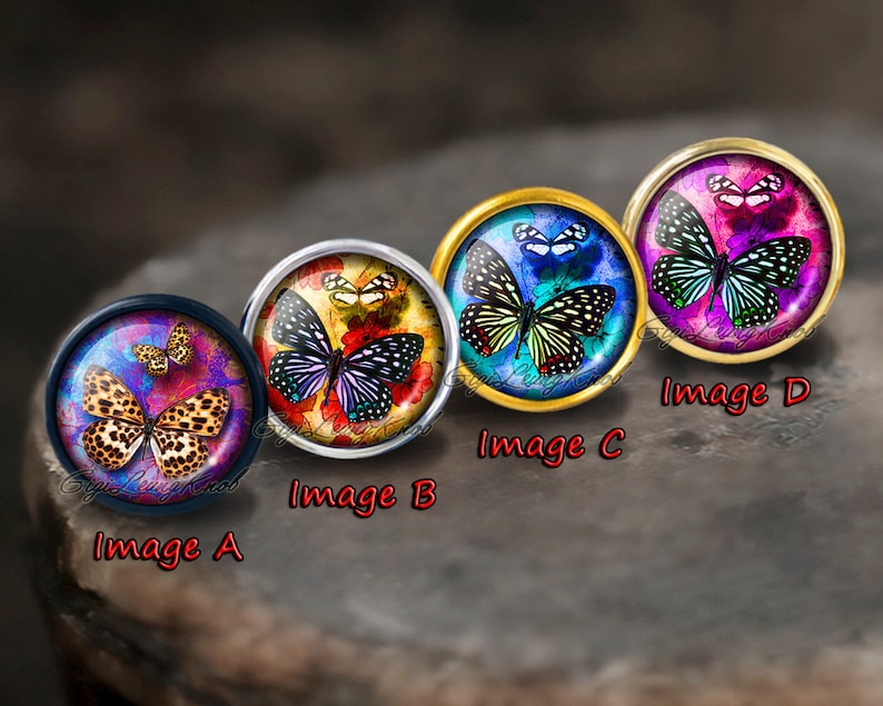 Pode incluir: Quatro caboch&otilde;es redondos de vidro com diferentes desenhos de borboletas. Os caboch&otilde;es est&atilde;o engastados em montagens de metal e est&atilde;o dispostos em fila. As borboletas s&atilde;o coloridas e t&ecirc;m detalhes intrincados. Os caboch&otilde;es s&atilde;o etiquetados como A, B, C e D.