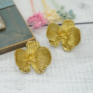 May include: A pair of gold flower-shaped earrings. The earrings are made of metal and have a textured surface.