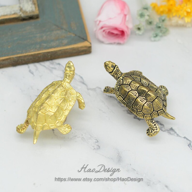 Peut inclure: Deux figurines de tortues dor&eacute;es. Une tortue est tourn&eacute;e vers l'avant, la t&ecirc;te lev&eacute;e, tandis que l'autre tortue est tourn&eacute;e vers l'arri&egrave;re, la t&ecirc;te baiss&eacute;e. Les deux tortues ont des motifs de carapace d&eacute;taill&eacute;s.