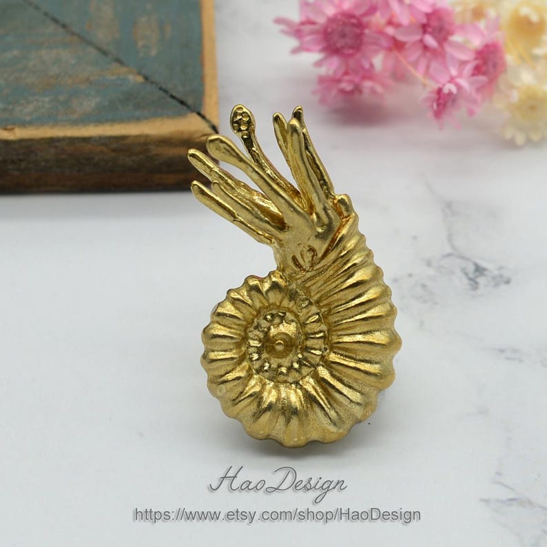 May include: A gold-coloured ammonite fossil with a detailed spiral design. The fossil is a decorative piece with a textured surface.