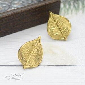 K&ouml;nnte beinhalten: Ein Paar goldene Ohrringe in Blattform. Die Ohrringe sind texturiert und haben ein detailliertes Blattdesign.