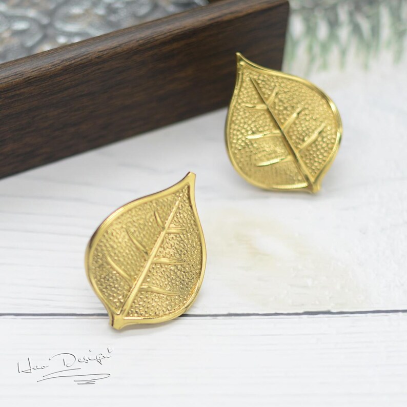 K&ouml;nnte beinhalten: Ein Paar goldene Ohrringe in Blattform. Die Ohrringe sind texturiert und haben ein detailliertes Blattdesign.