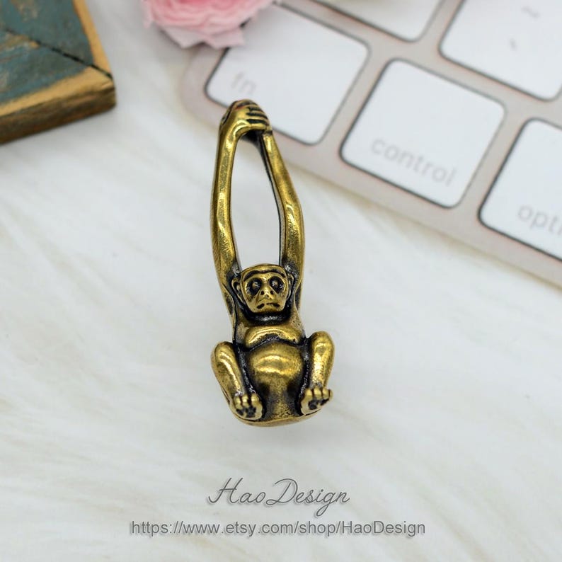 K&ouml;nnte beinhalten: Eine goldfarbene Metallfigur eines Affen, der an einem Ast h&auml;ngt. Der Affe sitzt mit erhobenen Armen &uuml;ber dem Kopf.