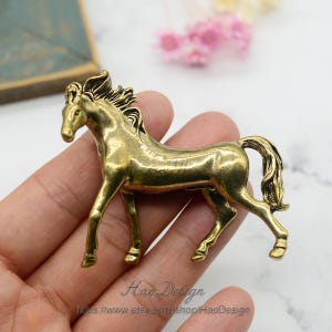 May include: A gold-toned metal horse figurine. The horse is standing on all four legs with its head held high. The horse has a flowing mane and tail.