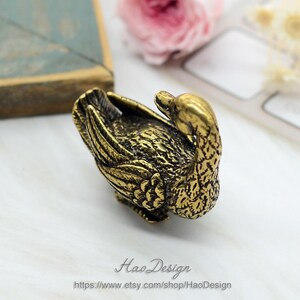 May include: A gold-coloured metal figurine of a goose with its head tucked under its wing. The goose is detailed with textured feathers and a realistic appearance.