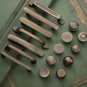 May include: A selection of antique brass cabinet handles and knobs in various sizes. The hardware has a warm, aged finish, and is arranged on a distressed green surface. The image includes the text "HaoDesign".