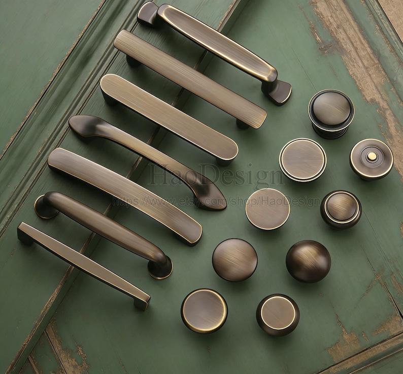 May include: A selection of antique brass cabinet handles and knobs in various sizes. The hardware has a warm, aged finish, and is arranged on a distressed green surface. The image includes the text "HaoDesign".