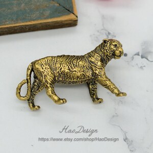 Pode incluir: Uma figurinha de tigre de metal dourado. O tigre est&aacute; andando com a cabe&ccedil;a virada para o lado. A figurinha &eacute; detalhada com listras e uma superf&iacute;cie texturizada.