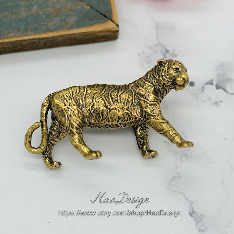Pode incluir: Uma figurinha de tigre de metal dourado. O tigre est&aacute; andando com a cabe&ccedil;a virada para o lado. A figurinha &eacute; detalhada com listras e uma superf&iacute;cie texturizada.
