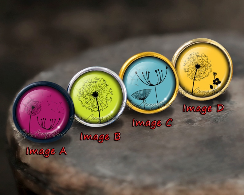 May include: Four round glass cabochons with black dandelion designs on different coloured backgrounds. The cabochons are set in silver and gold settings. The colours are pink, green, blue, and yellow.