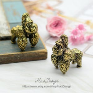 May include: Two gold-colored metal gorilla figurines. The gorillas are standing on a wooden surface. The gorillas are detailed with textured fur.