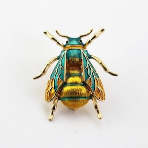 Op de afbeelding: Een gouden bij broche met groen en geel email. De bij heeft gedetailleerde vleugels en een textuurrijk lichaam.