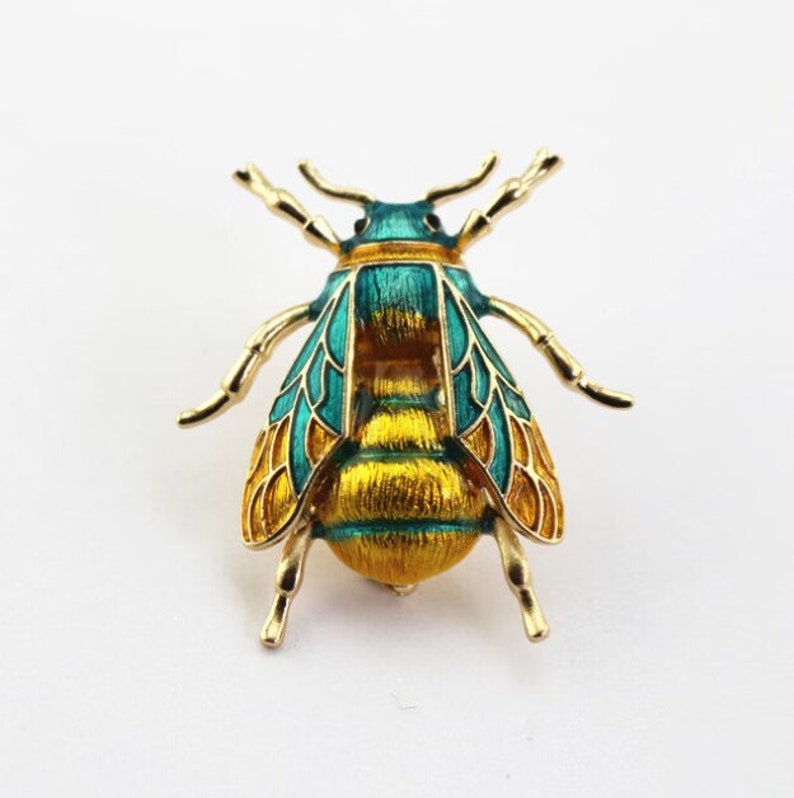 Op de afbeelding: Een gouden bij broche met groen en geel email. De bij heeft gedetailleerde vleugels en een textuurrijk lichaam.